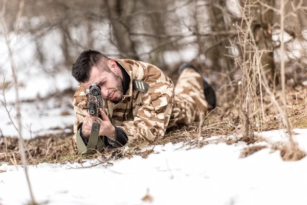 Military man in combat uniform holding a gun and shooting outdoors. Hunting or military concept