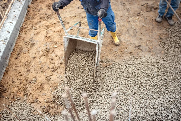 Construction worker carrying and unloading gravel and stones with wheelbarrow for foundation of building