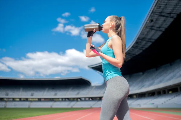 Portrait of healthy fitness girl drinking protein shake during workout on stadium