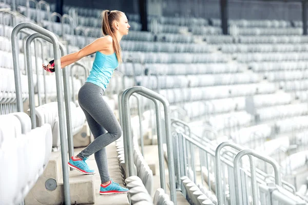 Fitness girl doing fitness exercises and working out on stadium stairs. Jogger on morning training, healthy lifestyle routine concept