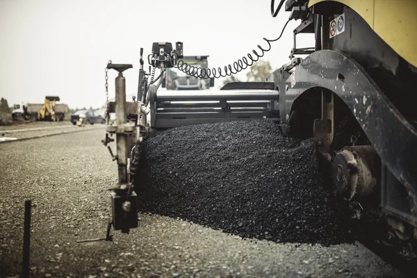 Paver machinery laying fresh asphalt or bitumen during road construction on building site. vintage, retro effect on photo