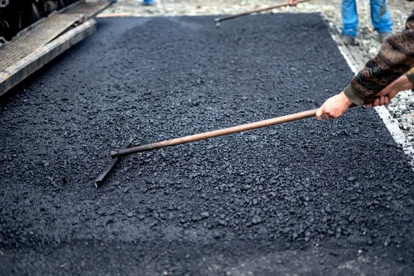 Worker leveling fresh asphalt on a road construction site, industrial building