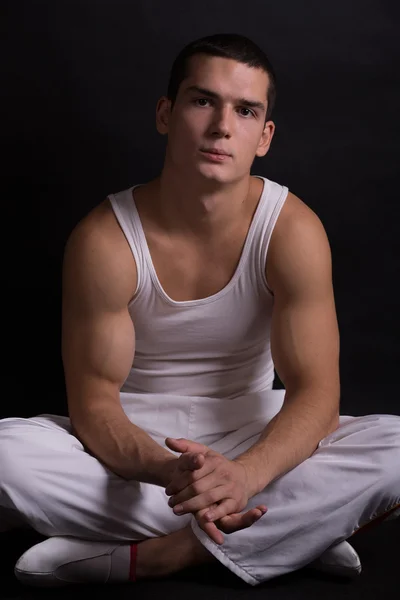 Beautiful young sporty muscular man in a white sports suit on a dark background. healthy body. strong muscles. big biceps. health. fitness. sports. Weightlifting