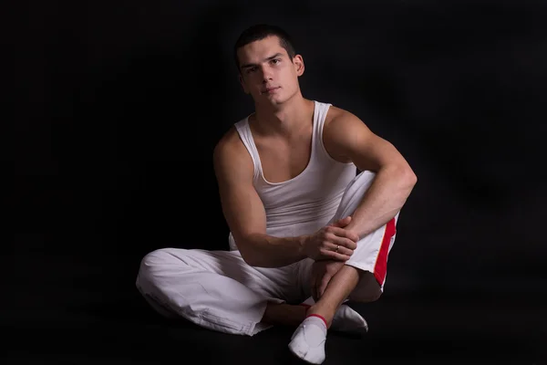 Beautiful young sporty muscular man in a white sports suit on a dark background. healthy body. strong muscles. big biceps. health. fitness. sports. Weightlifting