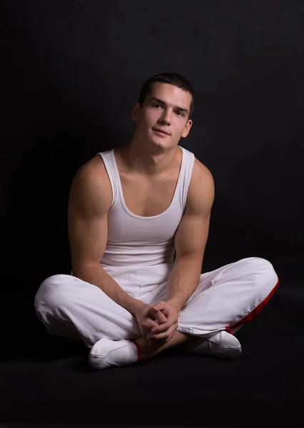 Beautiful young sporty muscular man in a white sports suit on a dark background. healthy body. strong muscles. big biceps. health. fitness. sports. Weightlifting