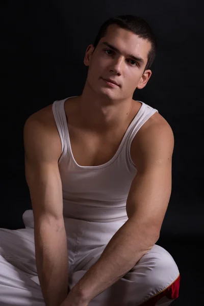 Beautiful young sporty muscular man in a white sports suit on a dark background. healthy body. strong muscles. big biceps. health. fitness. sports. Weightlifting