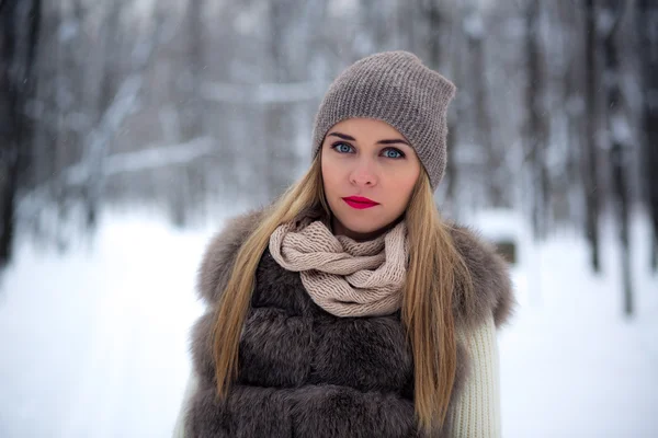 Stylishly dressed beautiful young girl in a fur vest walks in winter park