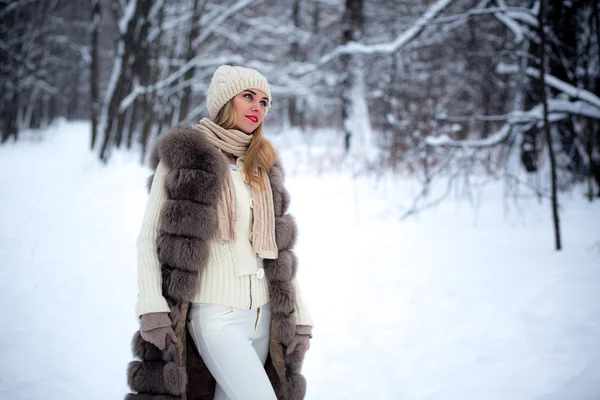 Stylishly dressed beautiful young girl in a fur vest walks in winter park