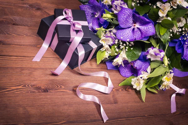 Gift with purple ribbon and a beautiful bouquet of white and purple flowers on a wooden background