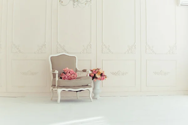 Luxury interiors in beige tones. Elegant vintage armchair in a spacious room with a wall decorated with ornaments. colorful flowers in a vase standing on the wooden floor