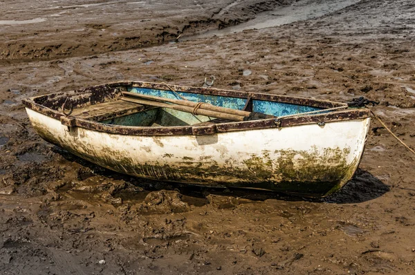 Single white rowing boat stuck on mud flats