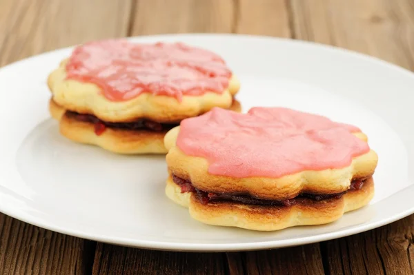 Two round sand cakes decorated with pink icing and jam on white