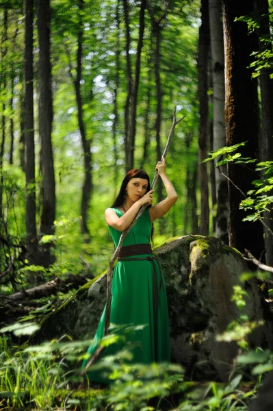 Slender young woman in straight green dress with stick in green