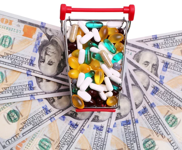 Shopping cart full with pills and capsules over dollar bills