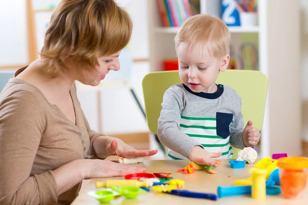 Kid boy and mother play colorful clay toy in nursery