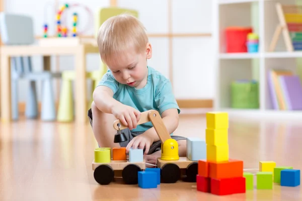 Child boy sitting on the floor and plays with building blocks and car
