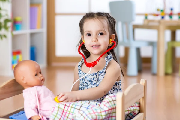 Kid toddler playing doctor role game examining her doll using stethoscope sitting in playroom at home, school or kindergarten