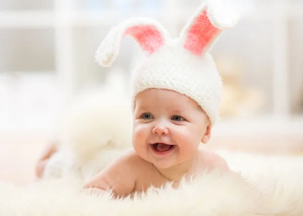 Smiling baby girl in rabbit costume lying on fur in nursery