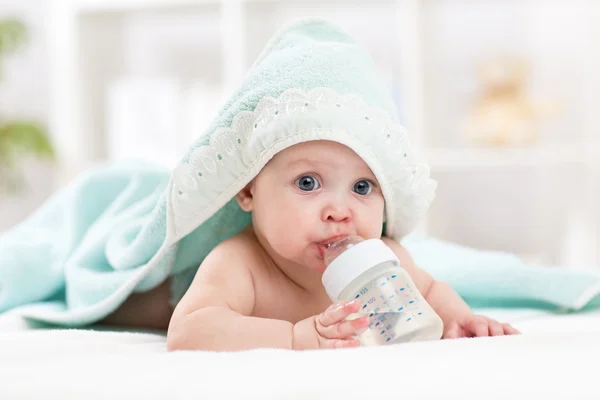 Happy baby girl drinks water from bottle wrapped towel after bath