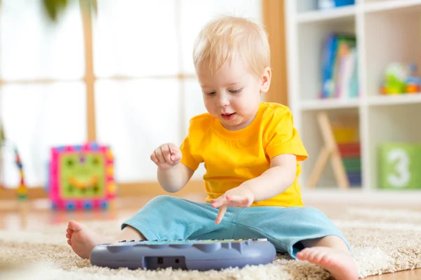 Happy kid boy playing piano toy in nursery