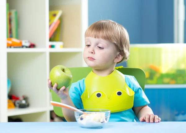 Child eating apple at dinner in nursery at home