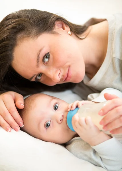 Cute mother at home feeding baby son with a milk bottle