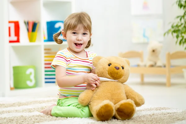 Child girl playing doctor with plush toy at home