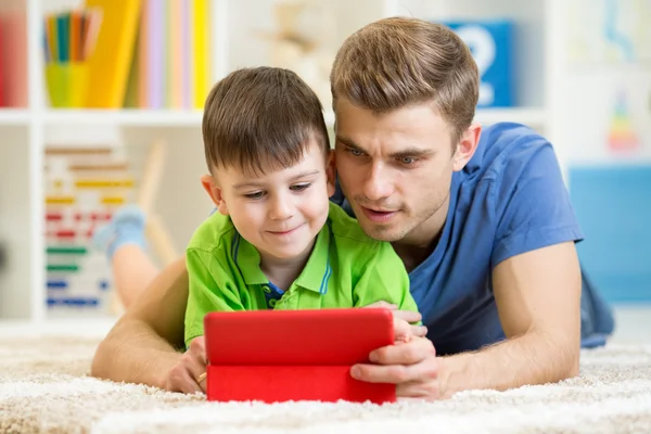 Dad and son kid play with tablet computer indoors