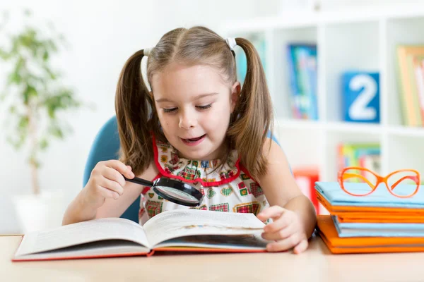 Astonished kid looking through a magnifying glass with book