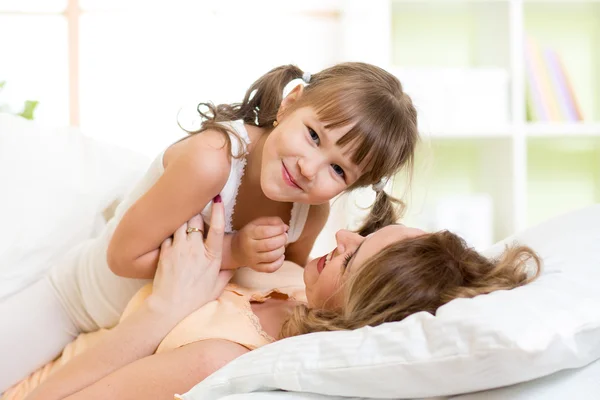 Mother and her child play and laugh in bed enjoying sunny morning in bedroom