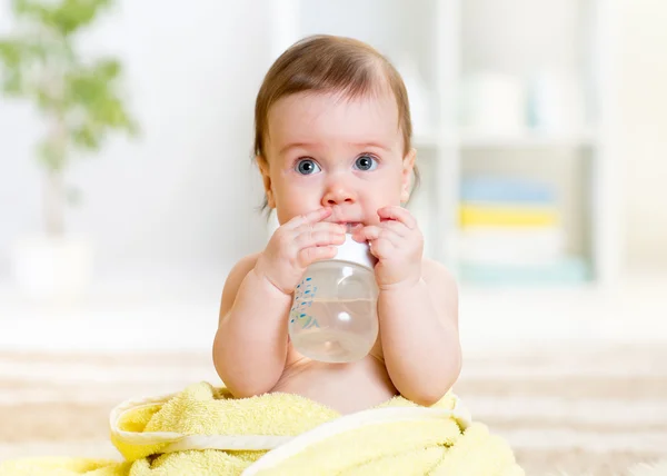 Baby drinks water from bottle sitting with towel