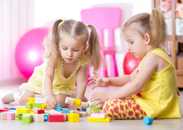 Children playing with wooden blocks sitting on the floor in room