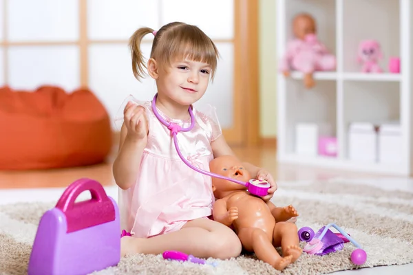 Little girl plays doctor examining a doll patient with toy stethoscope