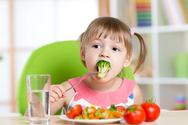 Cute little girl eats vegetable salad using fork