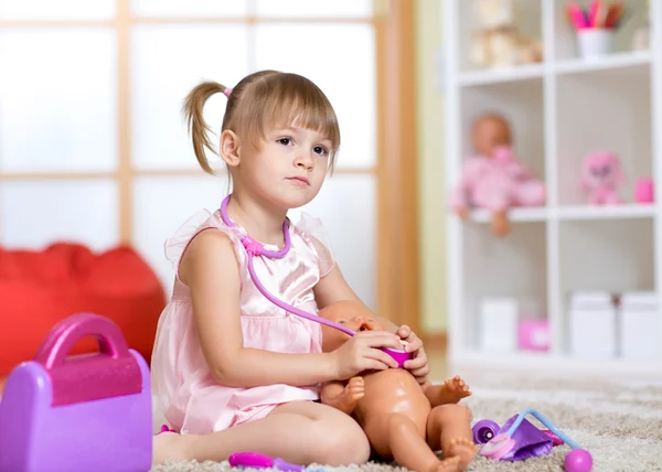 Small beautiful girl listens by means of stethoscope as heart of toy doll fights