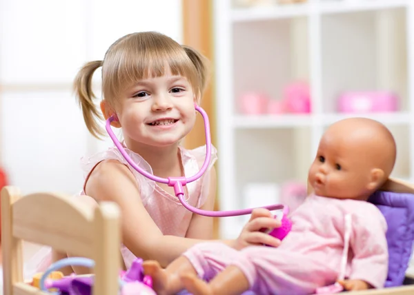 Child playing doctor role game examinating her doll using stethoscope sitting in playroom at home, school or kindergarten
