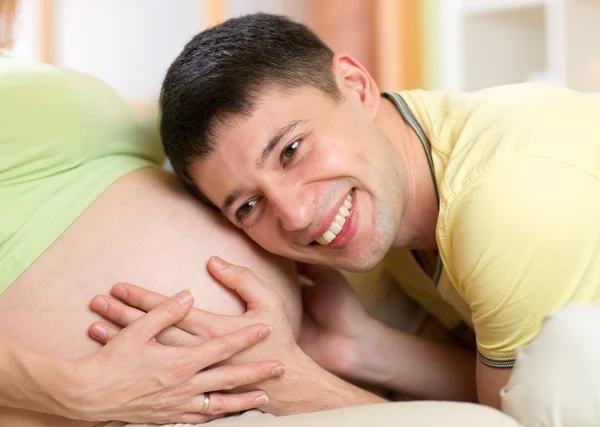 Happy man listening to belly of his pregnant wife