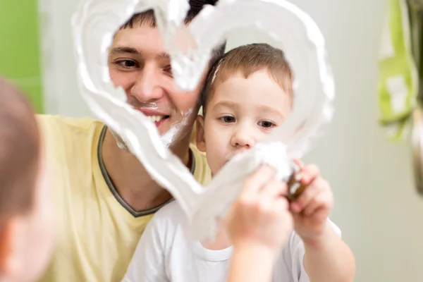 Father and son child draw heart shape on mirror with shaving foam playing in bathroom