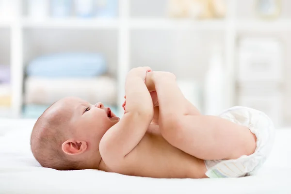 Baby playing with his feet lying on bed in nursery room
