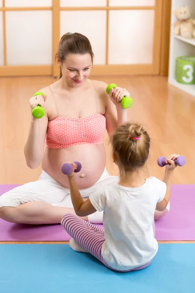 Pregnant woman and her elder child doing fitness exercises  with dumbbells