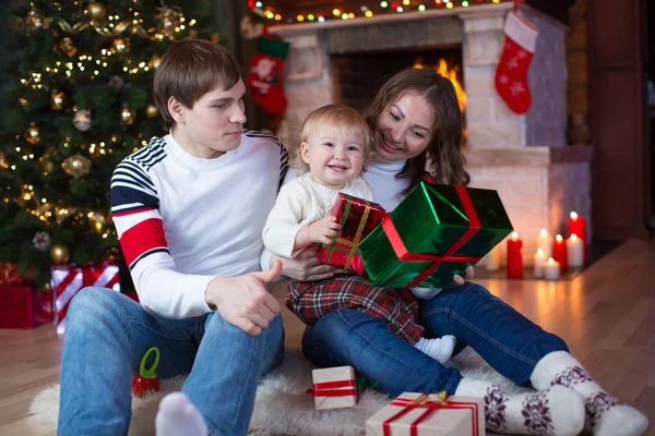 Happy family with gifts sitting at Christmas tree near fireplace