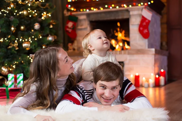 Happy family with little son lying near Christmas tree and fireplace