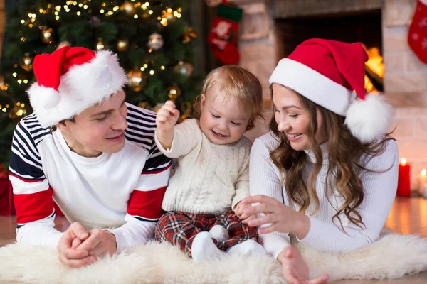 Happy family with little son lying near Christmas tree and fireplace