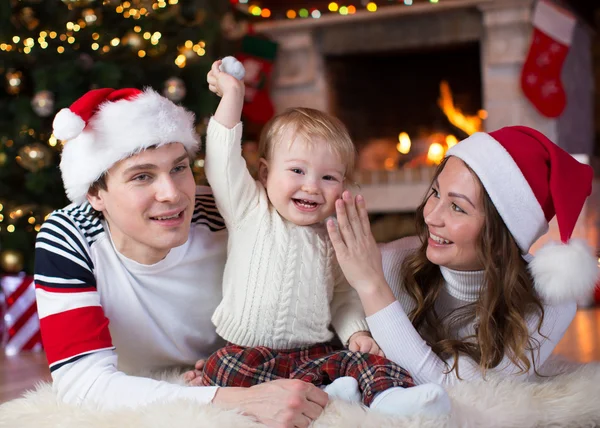 Happy family with little son lying near Christmas tree and fireplace