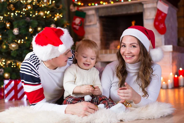 Happy family playing with little son lying near Christmas tree and fireplace