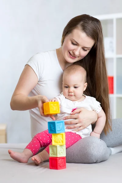 Mother and baby play with building blocks toy in nursery