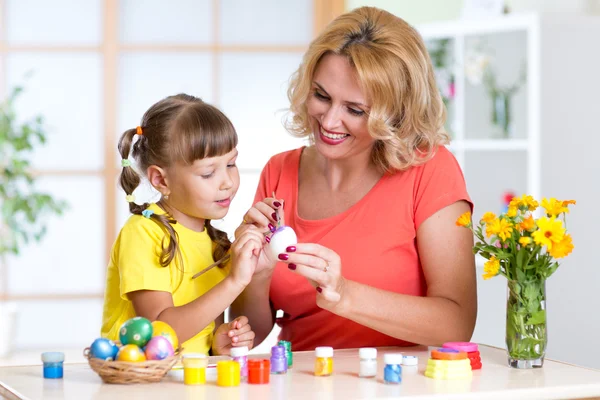 Happy mother teaches kid daughter to paint easter eggs