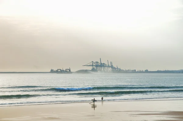 Surfer on the beach with industrial background