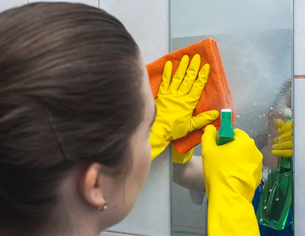 Woman with rag and spray cleaning the mirror