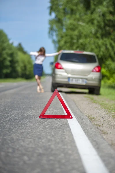 Red triangle warning sign and broken car on the road